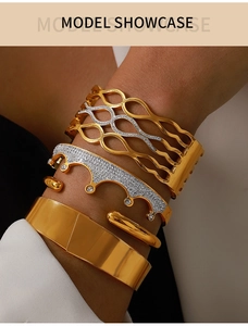 Model wearing a layered stack of gold-plated bracelets including crown and wave patterns