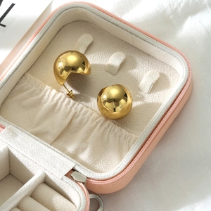 Detailed close-up of polished gold spherical stud earrings in a pink leather jewelry case