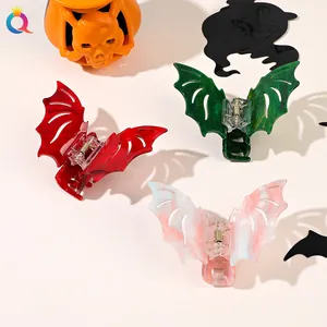 Three bat-shaped Halloween hair claws in marble and glitter finishes on festive background