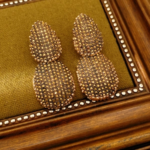 Dettaglio di orecchini pendenti vintage con pavé di cristalli champagne in oro lucido