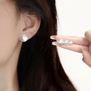 Close-up of classic round pearl stud earrings in three sizes shown with finger comparison