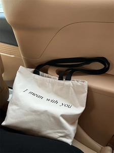 Close-up of beige canvas tote bag with 'I mean with you' print in car interior