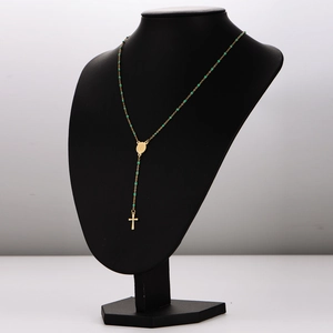 Goldene Rosenkranzkette mit grünen Perlen und Kreuzanhänger auf schwarzer Büste