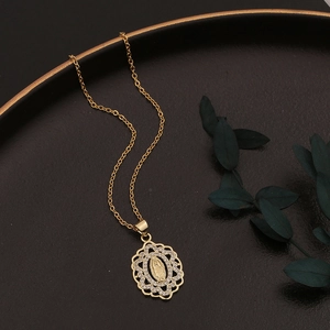 Elegant gold Virgin Mary necklace with crystal halo on dark textured plate with green leaves