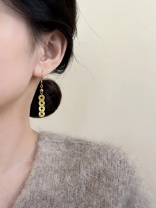 Detail of long gold copper coin earrings showing length and texture on model
