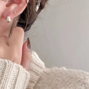 Close-up of minimalist silver teardrop earring worn on ear with high-polish finish