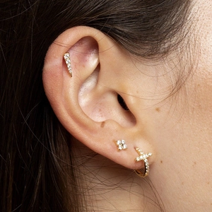 Golden cross hoop earring and zircon stud set shown on ear in a minimalist style