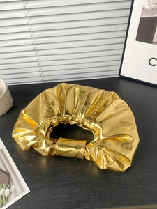 Detail of the golden metallic ruched cloud clutch bag with reflective pleated surface