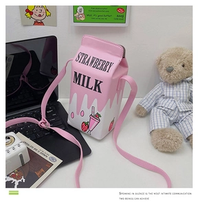Detail of pink strawberry milk carton crossbody bag with leather strap on a desk