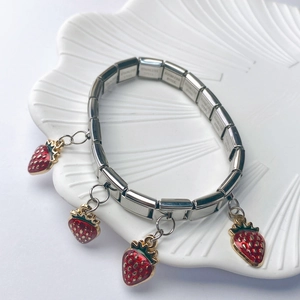 Detail of a red enamel strawberry charm on a polished stainless steel link bracelet