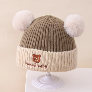 Detail einer Strickmütze mit Plüsch-Pompons und gesticktem Bärenmuster für Kinder