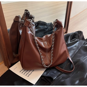 Detail view of brown leather hobo bag with silver metal chain strap and vertical stitching