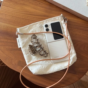 Detail of embroidered floral crossbody bag with leather strap on a wooden table