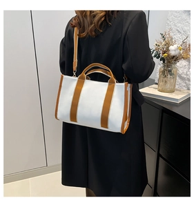 Canvas tote bag with brown trim shown styled on a shoulder over a long black wool coat
