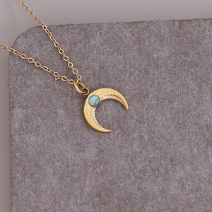 Macro view of gold crescent moon necklace with turquoise stone on stone background