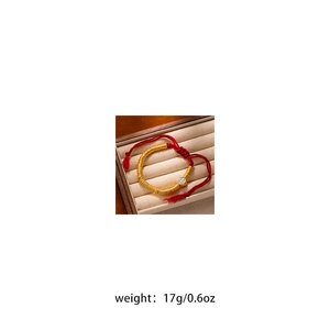 Detailed close-up of a gold charm red rope bracelet in a beige jewelry display box