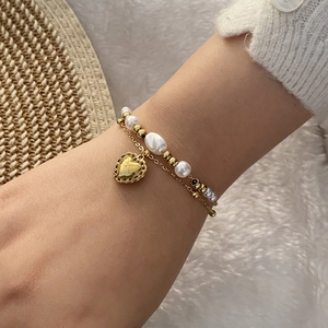 Bracelet double couche en perles avec pendentif cœur doré porté au poignet d'un modèle