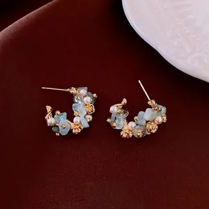 Elegant C-shaped aquamarine flower stud earrings with pearls on red silk fabric
