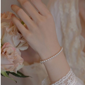 Detailed close-up of a 14k gold pearl bracelet worn on wrist against a lace background