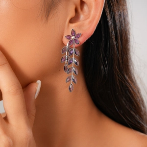 Detail of purple crystal flower and leaf tassel earrings worn on a model's ear