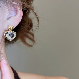 Dettaglio di orecchini a cuore placcati oro 18K con pendente leopardato indossati da modella