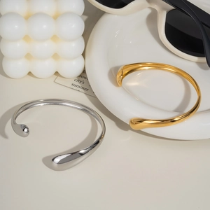 Minimalist wave open bangle in 18K gold and silver finishes on a ceramic plate