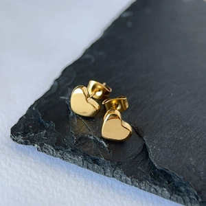 Close-up of polished gold heart stud earrings on a textured black stone surface