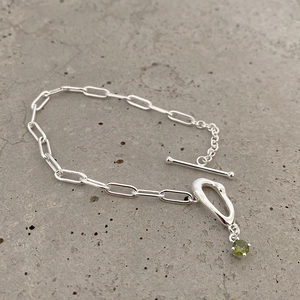 Detail view of silver chain bracelet featuring a T-bar clasp and green gemstone charm