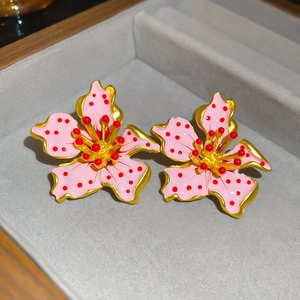 Close-up of pink floral earrings with red dots and golden metallic details on jewelry tray