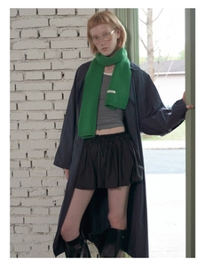 Detail of green knitted wool scarf featuring ribbed edges and a minimalist white tag
