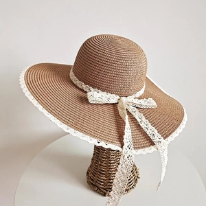 Dettaglio del cappello di paglia da donna con trama intrecciata e fiocco in pizzo bianco
