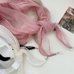 Detail of pink and white mesh scarves featuring pearl accents on a neutral surface