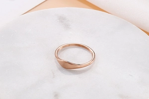 Close-up of rose gold minimalist signet ring with a polished mirror finish on marble stand