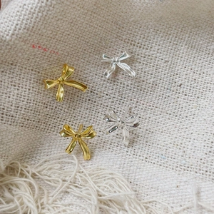 Detailed view of silver and gold bow earrings displayed on textured beige fabric