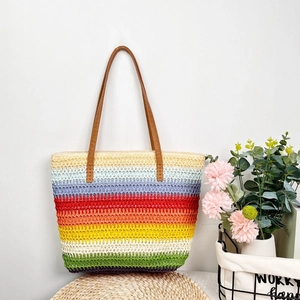 Detail shot of a colorful striped woven straw tote bag with brown PU handles on a woven mat