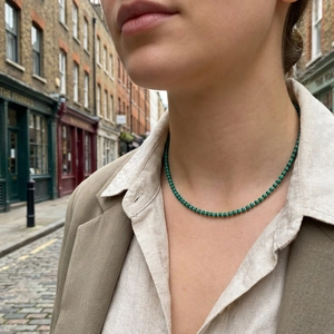 Handmade emerald green beaded necklace with gold accents worn by a model in a city street