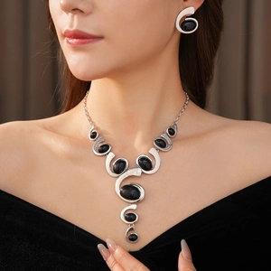 Close-up of model wearing silver swirl necklace and earrings set with black oval gemstones