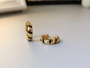 Macro detail of gold striped hoop earrings with black enamel zebra pattern finish