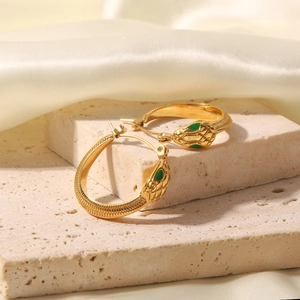 Detailed view of gold snake earrings with green gemstone eyes on silk and stone background