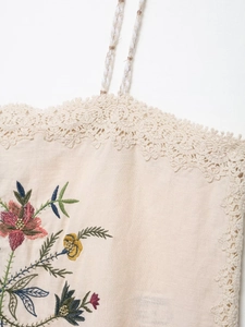 Detailed embroidery of colorful flowers and beige lace trim on a soft cotton fabric