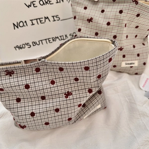 Detail of beige checkered makeup bag with red polka dots and a bow embroidery