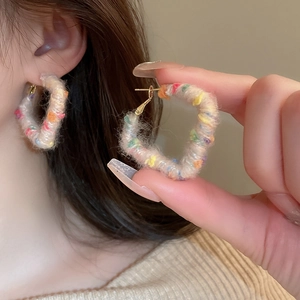 Detail showing heart-shaped plush earrings with colorful polka dots on a model ear