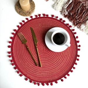 Detail of red woven coaster with gold thread and small pompoms on a set table