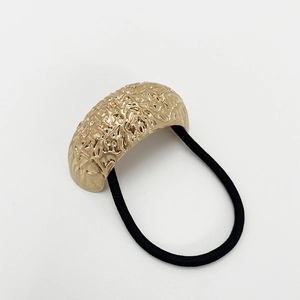 Close-up of golden hammered metal finish hair tie with black elastic cord on white background
