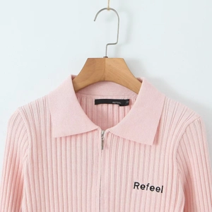 Détail du pull en maille côtelée rose avec col à revers, zip et broderie sur la poitrine