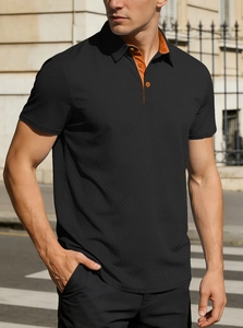 Détail d'un polo noir en maille gaufrée avec patte de boutonnage et col contrastés orange