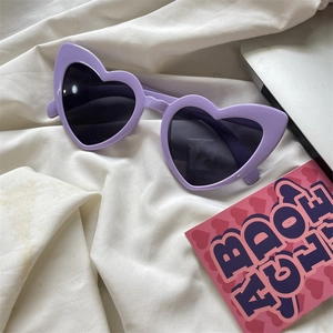 Detail of purple heart-shaped sunglasses on white fabric for trendy fashion styles