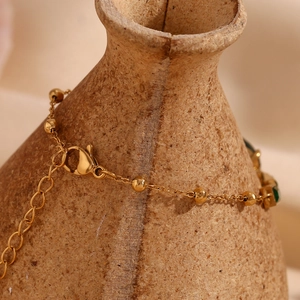 Détail d'un bracelet perlé plaqué or 18K avec pierres vertes sur céramique