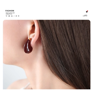 Close-up of deep red teardrop earrings with gold metal trim and glazed finish