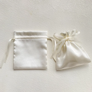 Detail of white satin drawstring gift bags with a glossy finish and elegant ribbon bows